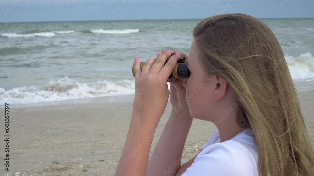 A girl looks at the sea through binoculars, the sea is stormy, the wind is blowing, alone on an island in the ocean is waiting for rescuers A girl looks at the sea through binoculars, the sea is stormy, the wind is blowing, alone on an island in the ocean is waiting for rescuers
