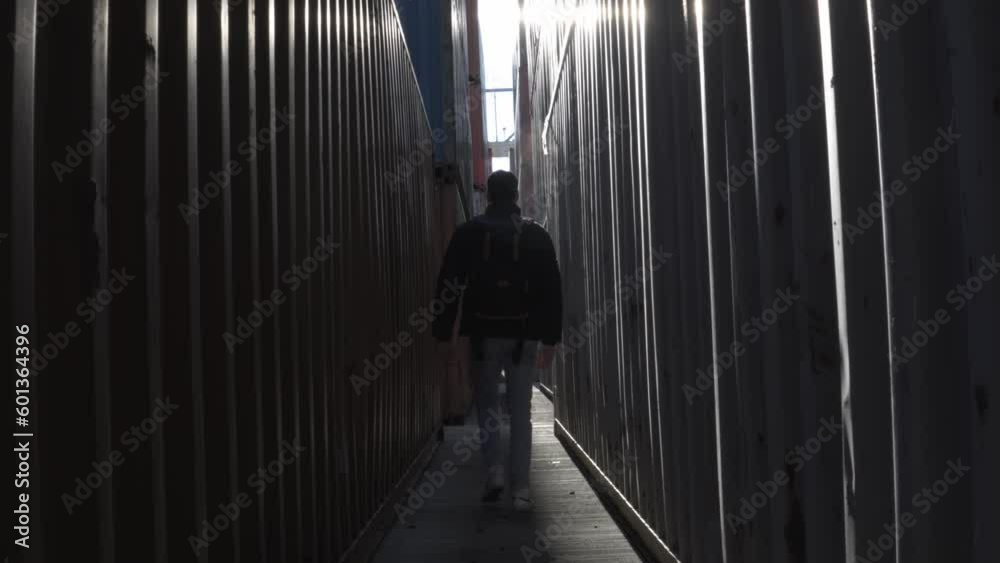 Low shot of a person walking with his back to the camera between containers, misting from the cold of the morning. Low shot of a person walking with his back to the camera between containers, misting from the cold of the morning.