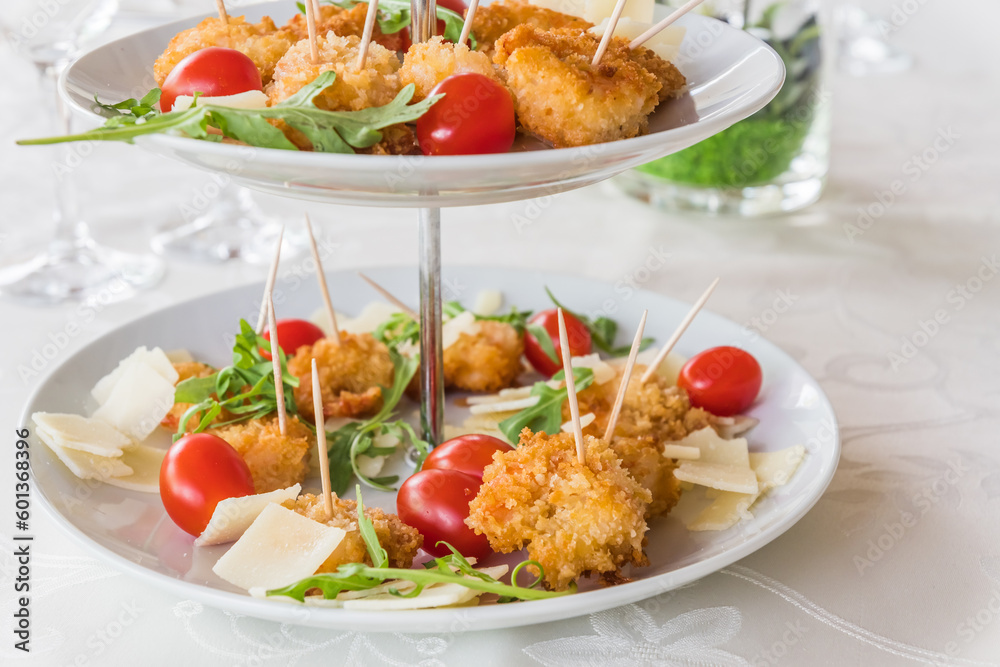 Fried breaded prawns with rocket salad on a porcelain cake stand on a white, elegantly set table Fried breaded prawns with rocket salad on a porcelain cake stand on a white, elegantly set table