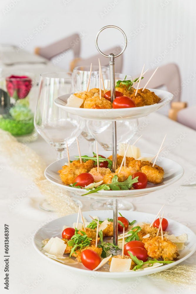Fried breaded prawns with rocket salad on a porcelain cake stand on a white, elegantly set table, vertical