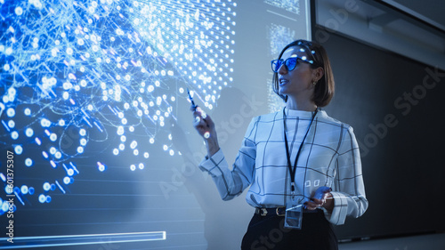 Young University Professor Explaining a Web Development Project to a Group of Students in a Dark Auditorium. Female Teacher Showing a Back-End Programmers Code on a Big Projector Screen photo