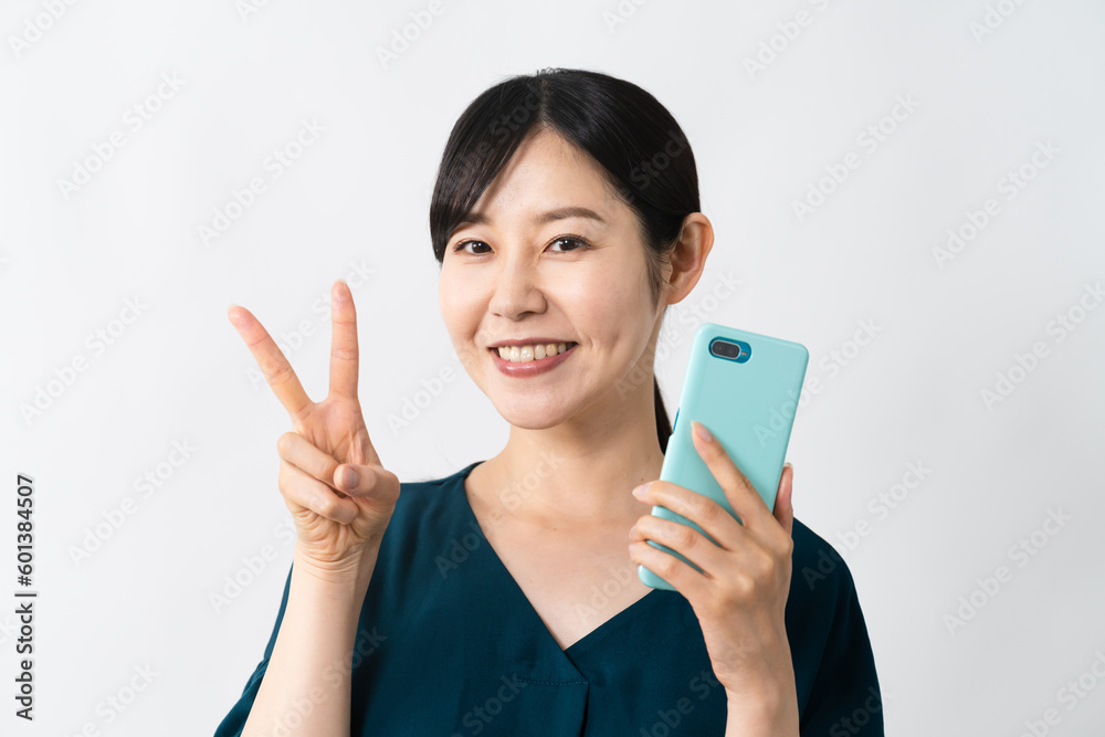 スマートフォンを持ちながらピースサインをする若い女性