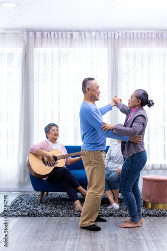 Senior friends on party dancing and playing guitar at home. Elderly musician at party has fun with cheerful family singing together. Leisure activity of Asian Senior.