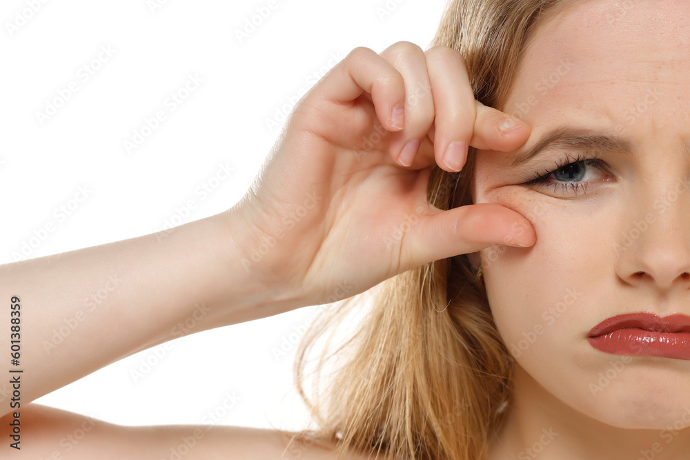 Fototapeta premium portrait of a young unhappy woman pinching her wrinkles next to her eyes on a white background