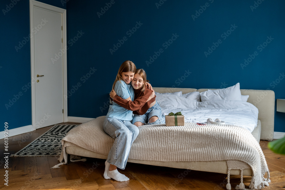 Happy teenage girl gently hugs beloved caring kind mother thanks for surprised birthday gift. Loving daughter embracing woman mom with tenderness while celebrating special occasion together at home. Happy teenage girl gently hugs beloved caring kind mother thanks for surprised birthday gift. Loving daughter embracing woman mom with tenderness while celebrating special occasion together at home.