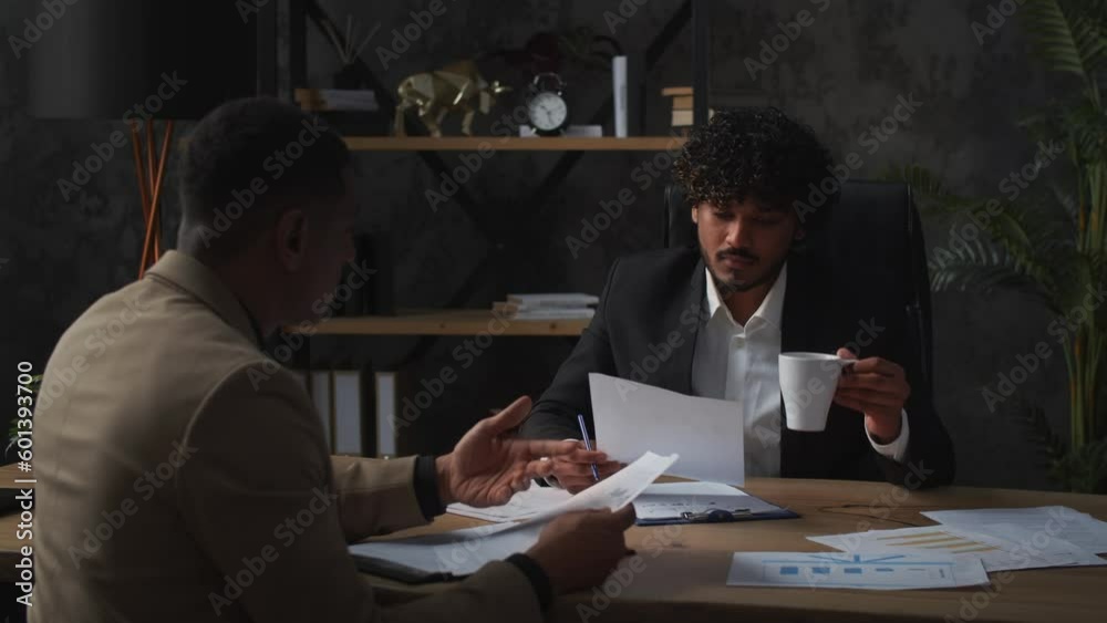 Two men in business suits are talking while sitting at a table and studying various documents. Directors of a financial company study reports for the last financial quarter. Two men in business suits are talking while sitting at a table and studying various documents. Directors of a financial company study reports for the last financial quarter.