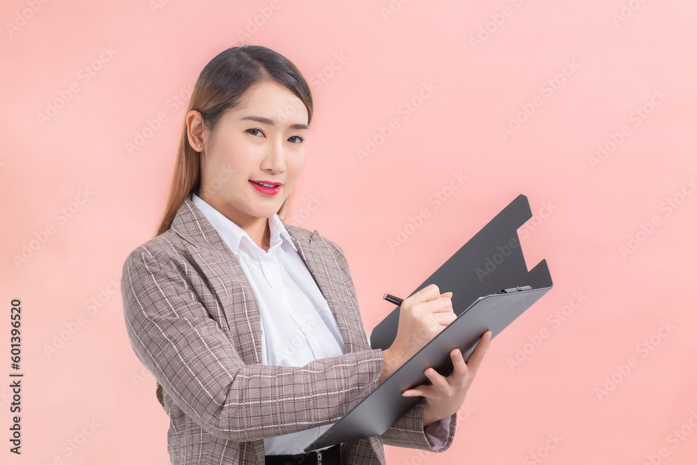 Professional Asian business women writing documents on the clipboard in hand while working at home isolated on peach color background. Professional Asian business women writing documents on the clipboard in hand while working at home isolated on peach color background.