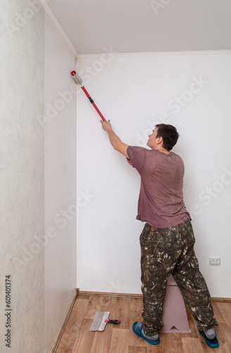 A worker applies wallpaper paste to the walls in a room with a roller