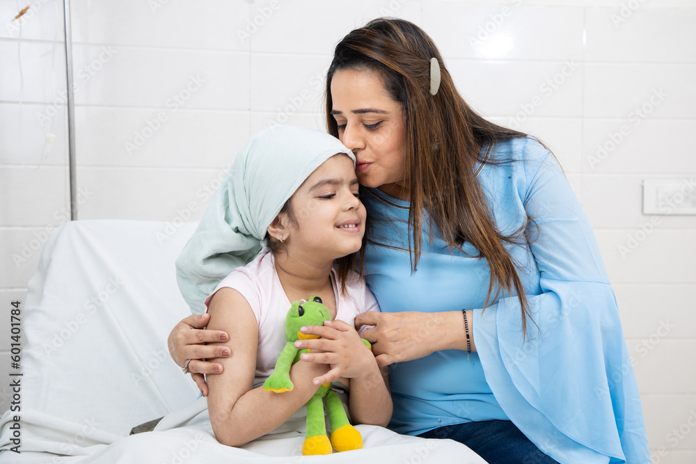 Indian woman hug and kiss her little daughter cancer patient undergoing course of chemotherapy in hospital. Health care concept. Indian woman hug and kiss her little daughter cancer patient undergoing course of chemotherapy in hospital. Health care concept.