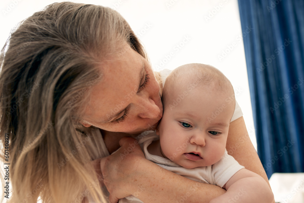 Mom hugs and kisses her little child in a bright child's room. Mom carefully holds the baby in her arms. Happy childhood Mom hugs and kisses her little child in a bright child's room. Mom carefully holds the baby in her arms. Happy childhood