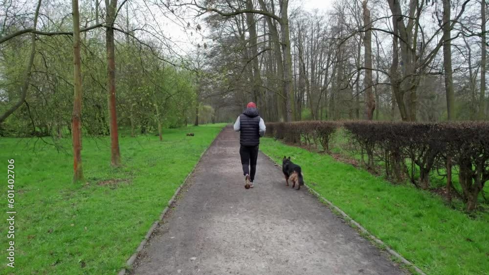 It's the beginning of spring, a man in a cap and vest walks his dog in a park, the cloudy sky above. It's the beginning of spring, a man in a cap and vest walks his dog in a park, the cloudy sky above.