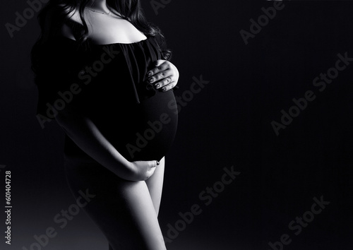 A pregnant woman in a black lingerie on a black background. Pregnant woman holds her belly. Pregnancy studio shoot. Copy space.