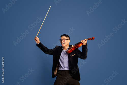 Portrait with professional, emotive musicians, violinist wearing costume holding fiddlestick and violin with happy face over blue studio background photo