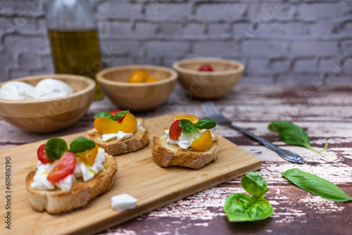 Tasty bruschetta with mozzarella, tomato, basil and oil. Background with bokeh effect. Bread on a wooden cutting board.