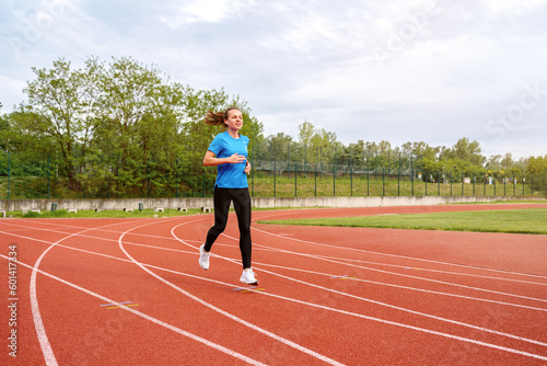 Woman runs on running track in stadium in summer.
