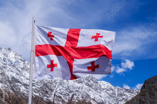 Foto Waving flag of Georgia against the background of snow-capped mountains and blue