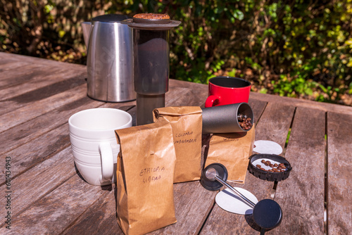 making cafe quality coffee at home: coffee grinder, coffee press, paper filters, sample bags  of coffee beans, kettle aand cups  on a wooden table top outside in sunshine photo