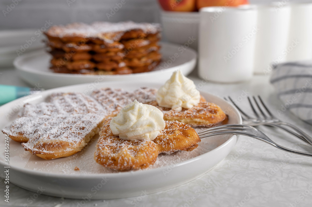 Fresh baked waffles with powdered sugar and whipped cream on kitchen table Fresh baked waffles with powdered sugar and whipped cream on kitchen table