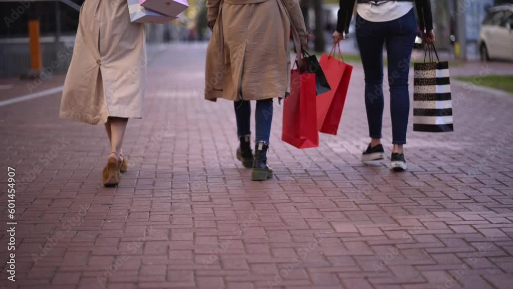 Rear view of three women walking outdoors holding shopping bags. Friends buying clothes and gifts on sale discounts. Rear view of three women walking outdoors holding shopping bags. Friends buying clothes and gifts on sale discounts.