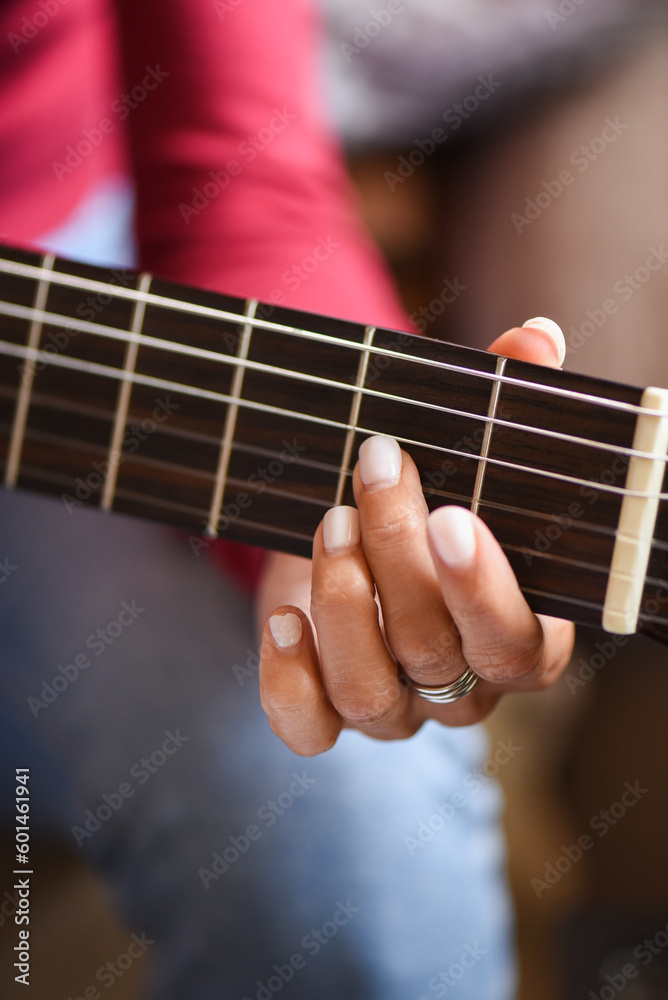 hand detail on the fret of a guitar, woman's fingers with white porcelain nails. Fuchsia pink jersey in the background, foreground detail of classical guitar.