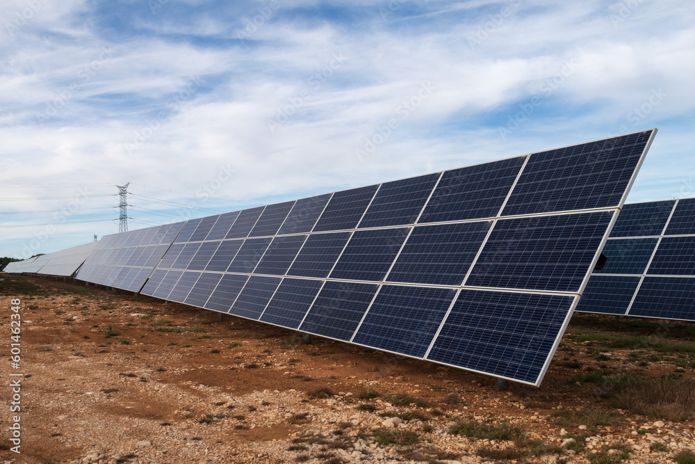 Vista de un huerto solar con sus placas solares y una torre eléctrica al fondo. Vista de un huerto solar con sus placas solares y una torre eléctrica al fondo.
