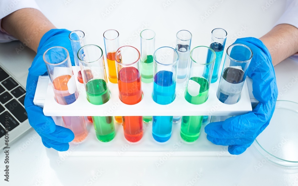 Fototapeta premium Row of colorful liquid chemical in test tube with scientist hand holding while wearing rubber blue gloves with laptop keyboard and sample tray in white lab