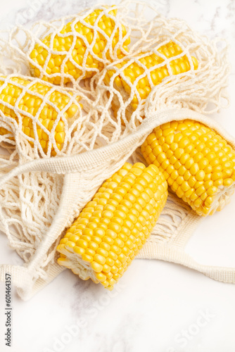 Mazorcas de maíz junto a una bolsa de red natural sobre un fondo de mármol blanco. Vista superior y de cerca. Copy space. Formato vertical photo