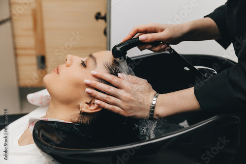 The hairdresser washes the head of a girl in a barbershop. brunette came for a haircut