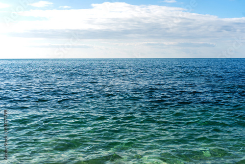 Blue sea water surface and horizon, blue sky and light clouds. Light ripples, waves on the sea.