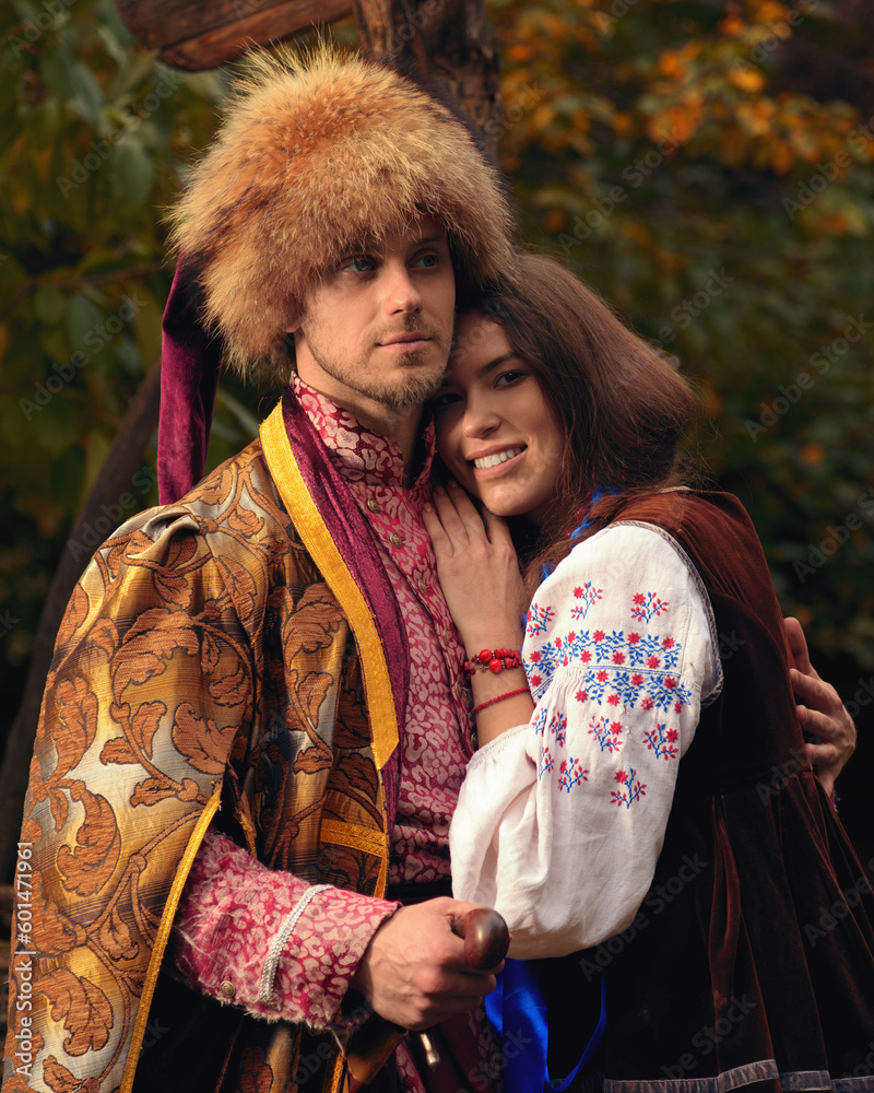 Young happy couple dressed traditional ukrainian clothing. Serious cossack man and smiling woman in embroidered costumes outdoors. Vintage outfit.