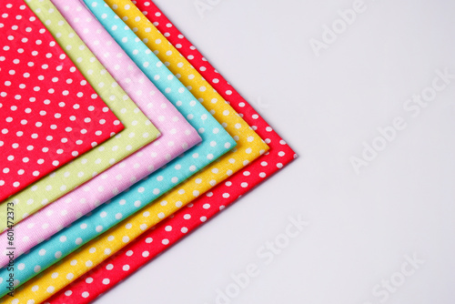 On a white background, bright multicolored patches of polka dot fabric lie on the ground.The concept of manual labor, a workshop for sewing and repairing clothes, a sale in a fabric store.Copyspace