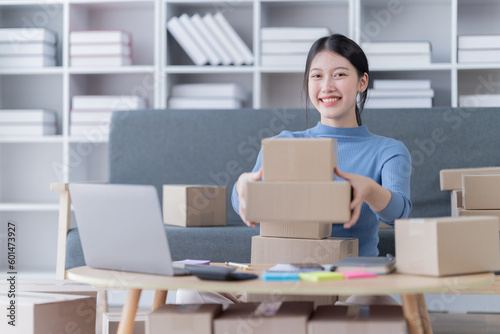 Asian business woman siting on sofa using a laptop and notebook checking order online shipping boxes at home. Starting SME Small business entrepreneur freelance. Online business, SME Work