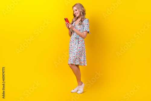 Full length photo of shiny adorable woman dressed flower print sarafan communicating modern device isolated yellow color background