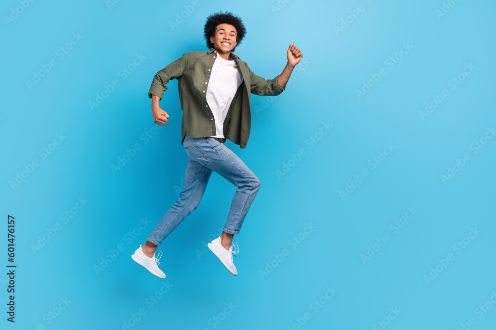 Full body photo of active young guy running wear khaki shirt denim jeans fast speed jumping positive isolated on blue color background