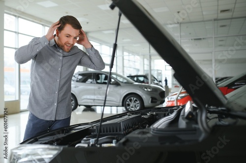 Looks under the hood of automobile. Young man in the car dealership.