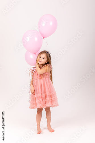 Cute smiling little girl in a pink princess dress posing with air balloons isolated on white background. Kids Birthday party celebration concept. Happy Birthday banner with copy space. Studio shot.