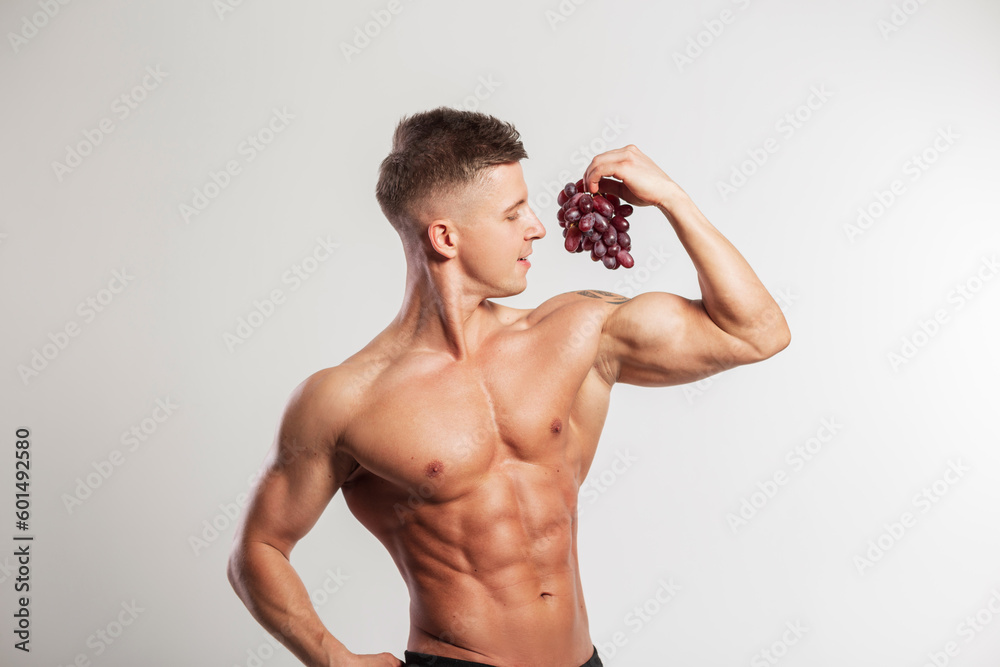 Cool strong muscular handsome man with a muscular body holds grapes and shows a bicep on a white background. Vitamins and fruits