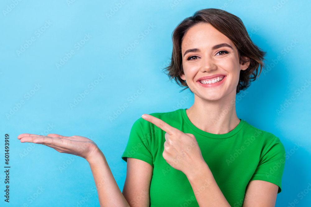 Portrait of toothy beaming smiling lady wear stylish t-shirt hold arm finger point mockup new stomatology name isolated on blue color background Portrait of toothy beaming smiling lady wear stylish t-shirt hold arm finger point mockup new stomatology name isolated on blue color background