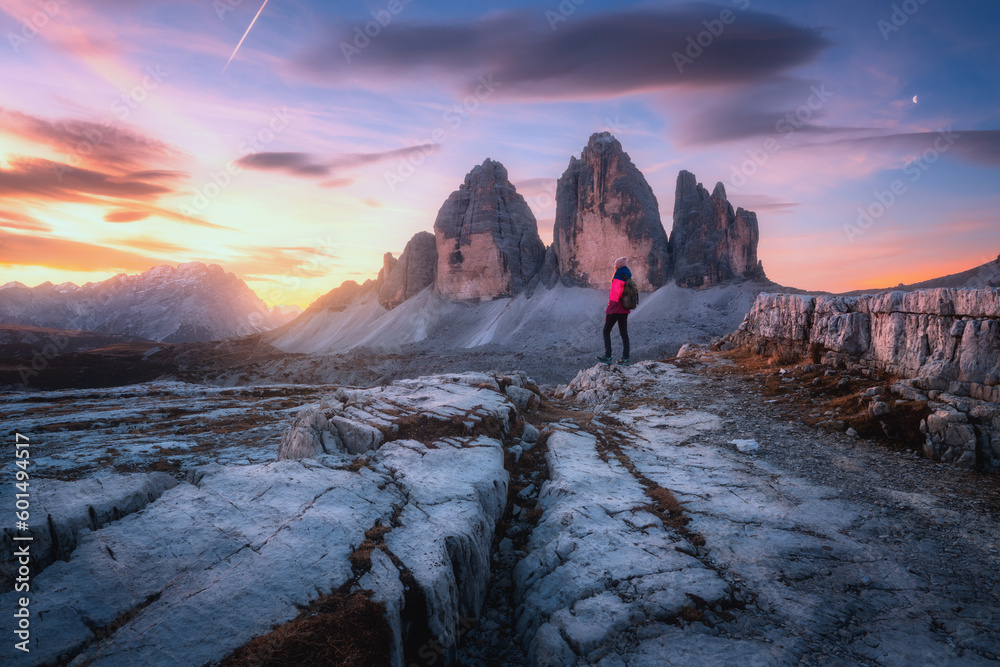 Woman on the mountain trail and high rocks at colorful sunset in autumn. Tre Cime, Dolomites, Italy. Beautiful landscape with girl on path, cliffs, purple sky with pink clouds in fall. Hiking. Travel - obrazy, fototapety, plakaty 