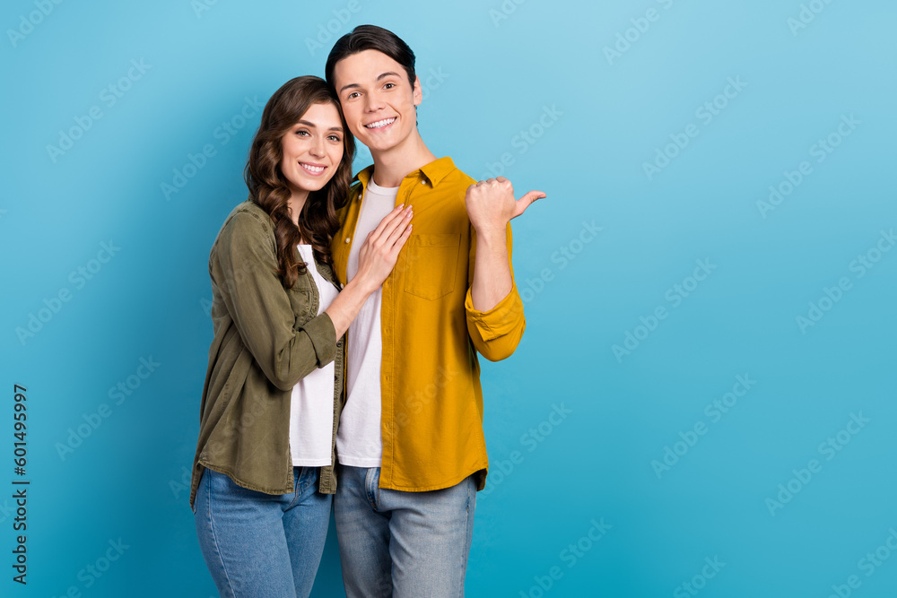 Photo of dreamy sweet married couple wear shirts pointing thumb empty space isolated blue color background Photo of dreamy sweet married couple wear shirts pointing thumb empty space isolated blue color background
