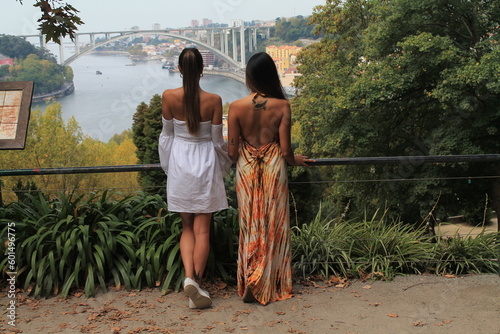Exploring the Scenic Waterfront of Porto: Photo of Two Young Women with Long Hair Sightseeing by the River and Bridge