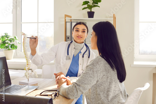 Tableau sur toile Portrait of female doctor physiotherapist or orthopedist showing to her woman patient model of spine in her office giving consultation about scoliosis or spinal problems during medical exam