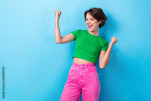 Photo of young screaming funny girl wear green t-shirt pink trousers hooray fists up celebrate victory yelling isolated on cyan color background