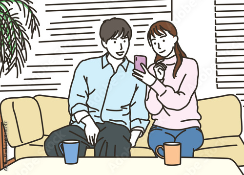 ソファーでスマートフォンを見るカップル