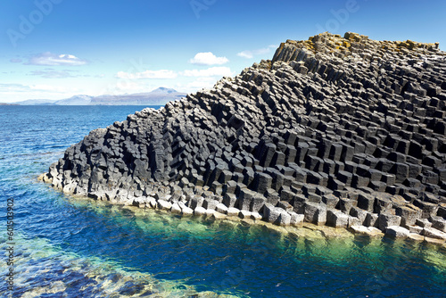 Isle of Staffa, Scotland: dark hexagonal basalt columns in the turquoise waters of the Inner Hebrides against a blue summer sky.