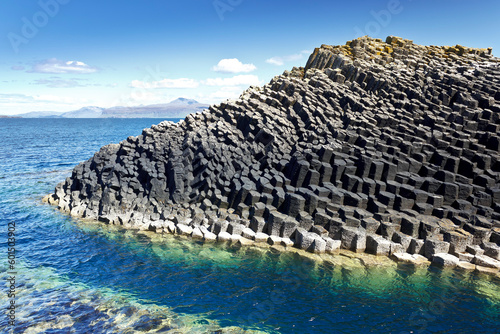 Isle of Staffa, Scotland: dark hexagonal basalt columns in the turquoise waters of the Inner Hebrides against a blue summer sky. photo