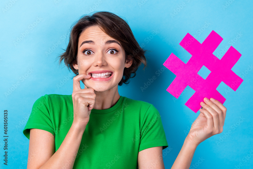 Portrait of excited young girl bite nail anticipation hold paper hashtag social media share her new photo instagram isolated on cyan color background Portrait of excited young girl bite nail anticipation hold paper hashtag social media share her new photo instagram isolated on cyan color background