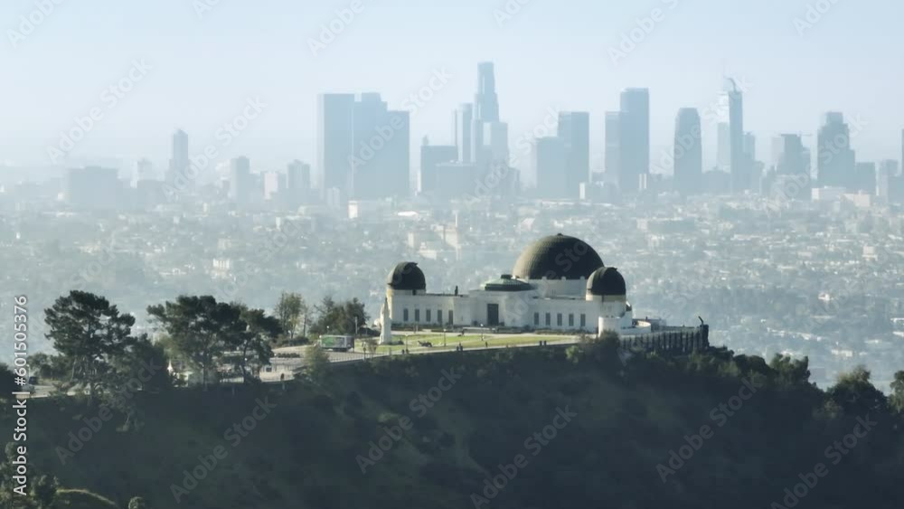 Breathtaking view Griffith Observatory Domes on Mount Hollywood on sunny summer day with downtown Los Angeles skyscrapers on motion background. Aerial Los Angeles cityscape California USA March 2023