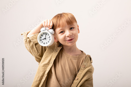 A portrait of kid boy holding white alarm clock. Children and time management concept