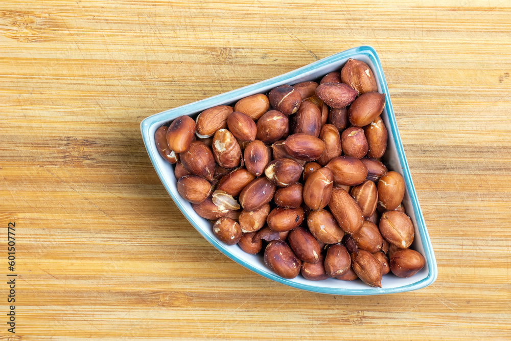 Obraz premium Roasted peanuts in a plate on a wooden kitchen board.